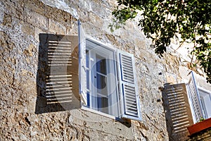 White window with open white window blinds (window shutters) in one of the old streets in Mdina, historic Malta capital