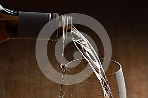 White wine Being Poured into Glass. Stream of wine from bottle and swirls and bubbles in glass. Glass with golden liquid on wooden