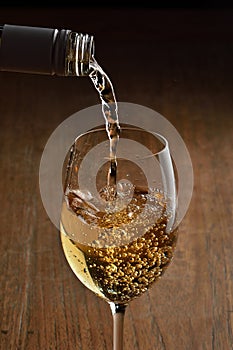 White wine Being Poured into Glass. Stream of wine from bottle and swirls and bubbles in glass. Glass with golden liquid.