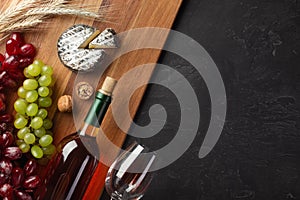 White wine bottle, bunch of grapes, cheese, ears of wheat and wineglass on wooden board and black background