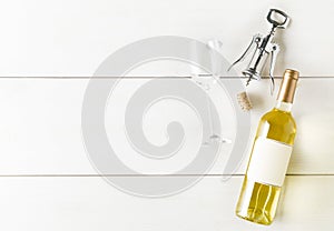 White wine bottle with corkscrew, cork and wine glass on white wooden table flat lay from above