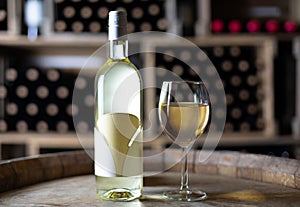 white wine bottle with a filled wineglass on a barrel in a cellar