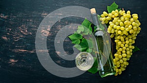 White wine in a bottle with a glass and grapes. On a black wooden background. Free space for text.