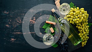 White wine in a bottle with a glass and grapes. On a black wooden background. Free space for text.