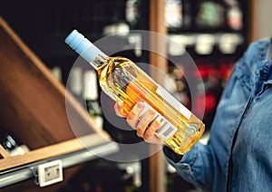 White wine bottle in hand in liquor store. Customer buying alcohol. Woman choosing the right bottle of chardonnay or riesling.