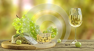 White wine, cheese and grapes on wooden table with blurred wineyard in background