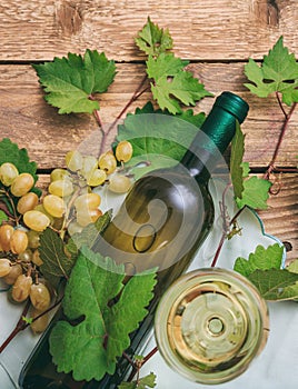 White wine glass and bottle and fresh grapes on wooden background