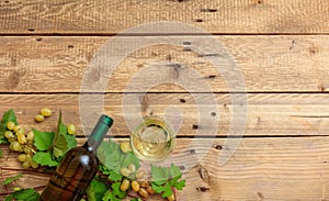 White wine glass and bottle and fresh grapes on wooden background, copy space