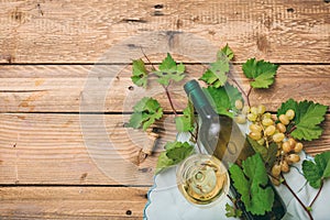 White wine glass and bottle and fresh grapes on wooden background, copy space