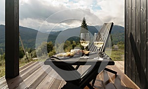 White wine glasses and plate of cheese on terrace with mountains view with copy space