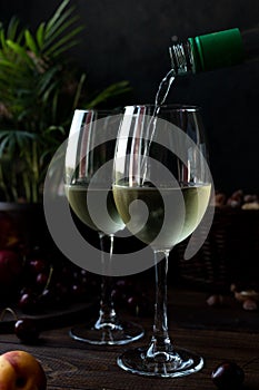 White wine is poured into glasses. There are fruits nearby