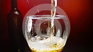 White wine pouring into a wine glass on red background in slow motion