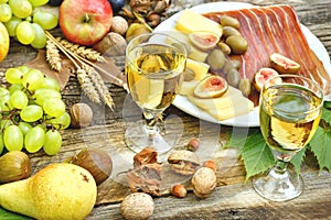White wine, prosciutto, cheese and seasonal fruits on rustic table