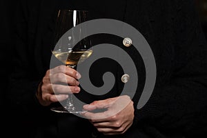 White Wine Tasting Tour, glass close up, teenage girl hands with a black knitted coat as background.
