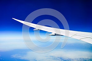 White wing of the aircraft view from airplane window seat flying in the blue sky with white clouds background over the ocean