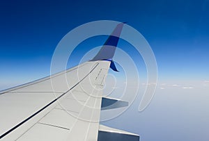 White wing of a passenger plane against a clear blue sky