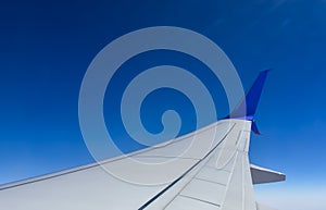 White wing of a passenger plane against a clear blue sky
