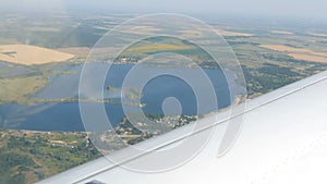 The white wing of a passenger plane against the top view of nature backdrop of a beautiful blue lake, flies over a pond