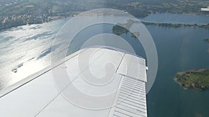 The white wing of a passenger plane against the top view of nature backdrop of a beautiful blue lake, flies over a pond