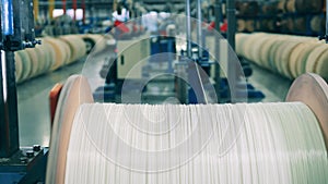 White wire unwinding from a large wooden spool at a factory. Industrial equipment at modern factory facility.