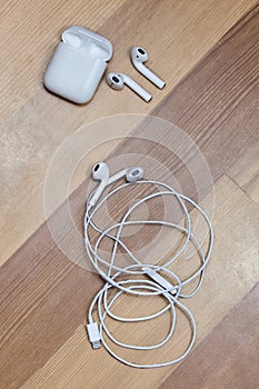 White wire and wireless earphones on wooden background with charger box, chosen focus.