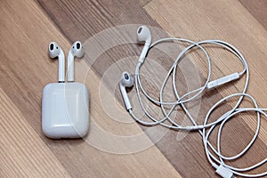 White wire and wireless earphones on wooden background with charger box, chosen focus.