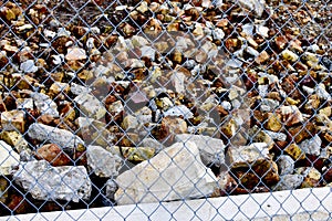 White wired fence with colorful stones and leaves behind it under sunlight