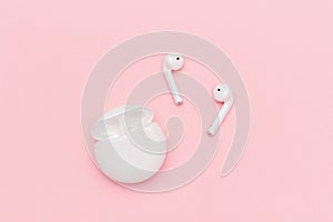 White wireless Bluetooth headphones and charging case on pink paper background