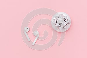 White wireless Bluetooth headphones and charging case on pink paper background. Template for text or your design. Flat lay Top
