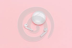 White wireless Bluetooth headphones and charging case on pink paper background. Template for text or your design. Flat lay Top