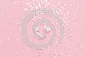 White wireless Bluetooth headphones and glitter confetti on pink paper background. Template for text or your design. Flat lay Top