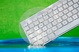 White wireless computer keyboard falling into the water spraying