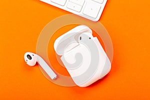 White wireless earphones with charging case on bright orange background