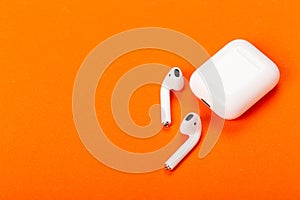 White wireless earphones with charging case on bright orange background