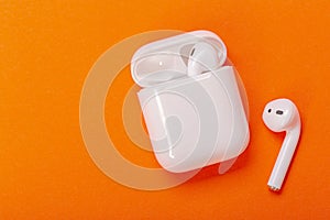 White wireless earphones with charging case on bright orange background