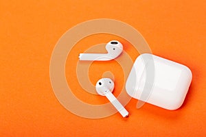 White wireless earphones with charging case on bright orange background