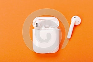 White wireless earphones with charging case on bright orange background