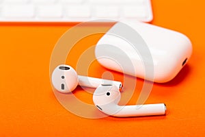 White wireless earphones with charging case on bright orange background