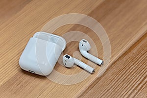 White wireless earphones on wooden background with charger box, chosen focus.