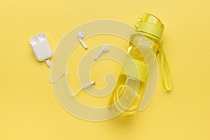 White wireless headphones and a bottle with a refreshing drink on a yellow background