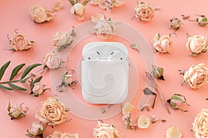White wireless headphones in the case on playful pink background with delicate dry roses flowers