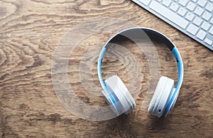 White wireless headphones and computer keyboard on wooden desk.