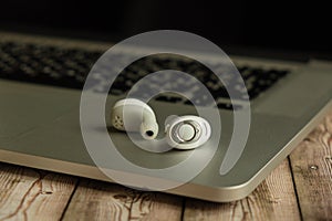 White wireless headphones and laptop on a wooden background