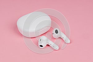 White wireless headphones on pink background. New earphones. New technologies