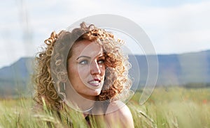 white woman in black dress with gold detail, curly hair, looking at the horizon