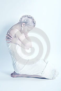 White woman sitting alone in white room