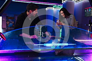 White woman taking photo on cellphone while playing air hockey