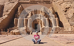 White Woman Tourist in front of the Colossal Statues of Ramesses II seated on throne near the entrance to Great Temple Abu Simbel