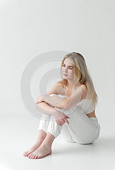 White woman in white sweatpants and top sitting on white floor ,blonde