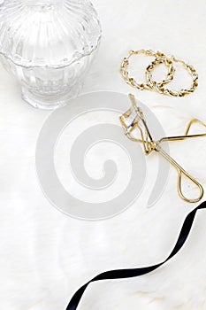 White women cosmetic desk decorated with glass vase earrings and eyelash curler background